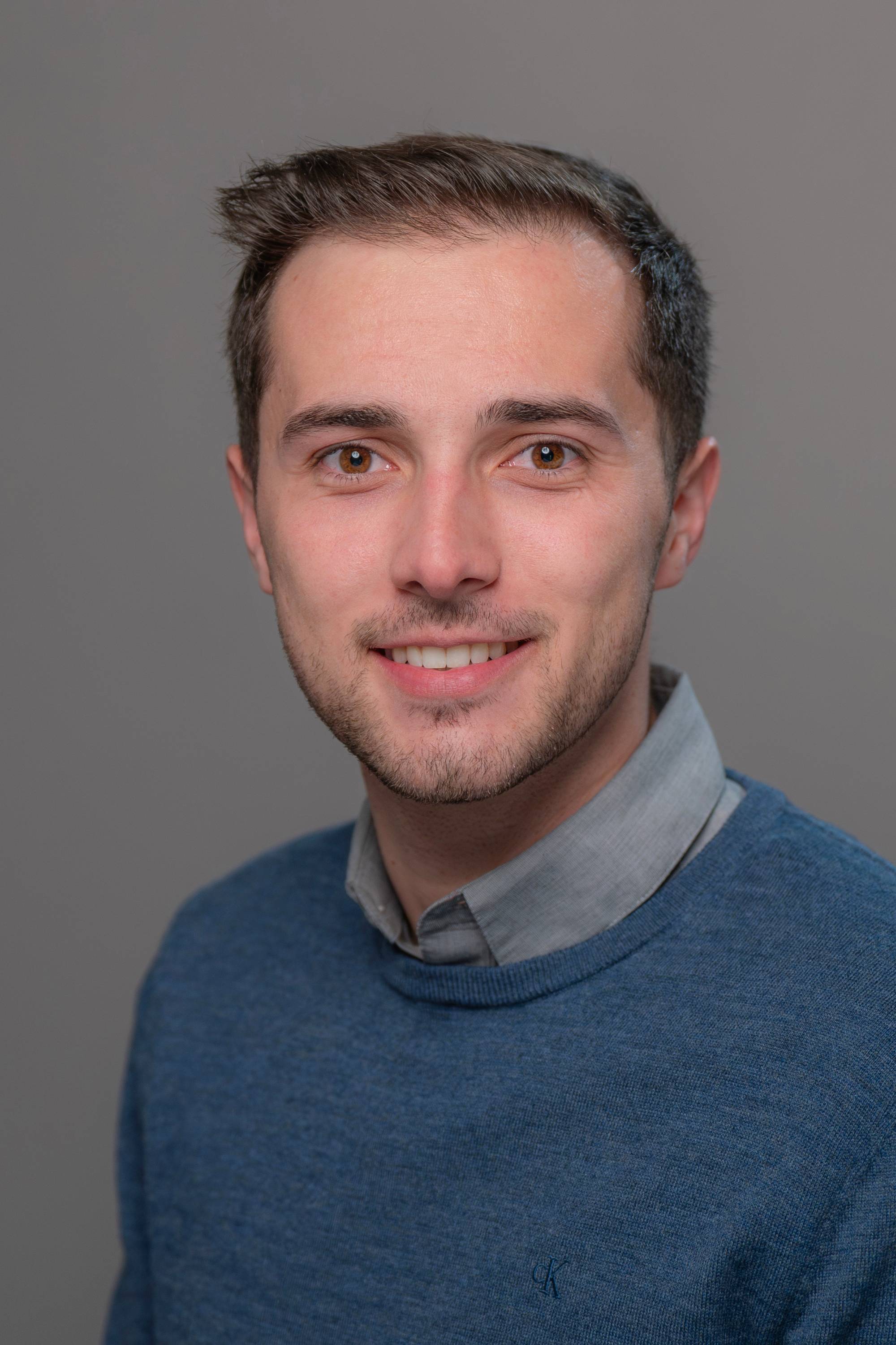 Damian Martinez portrait photo with a blue sweater and gray backdrop